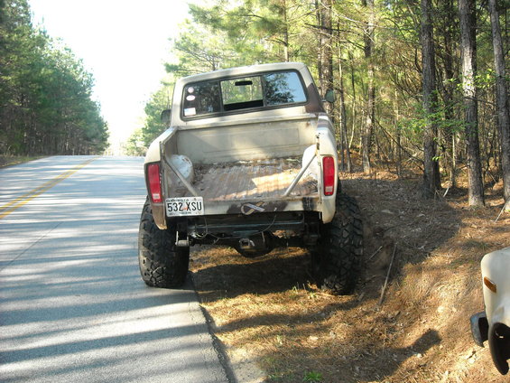 Rear view of a 1979 Ford F-150 parked on a dirt shoulder next to a road