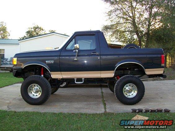 Lifted dark blue Ford Bronco with tan trim, side view. Shows 'Bronco' badge on fender