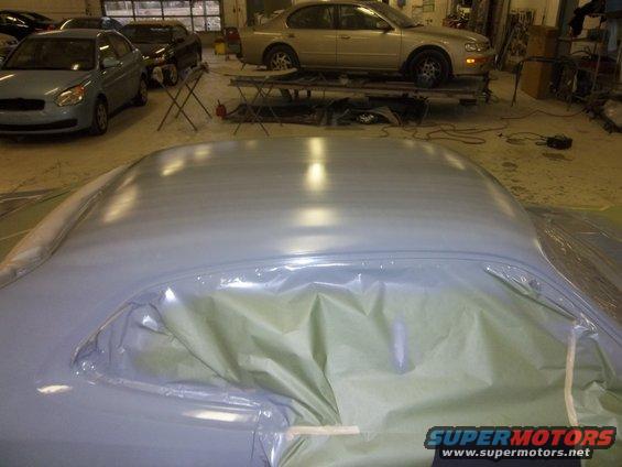 Car roof covered in plastic sheeting, ready for paint. Other cars in shop background