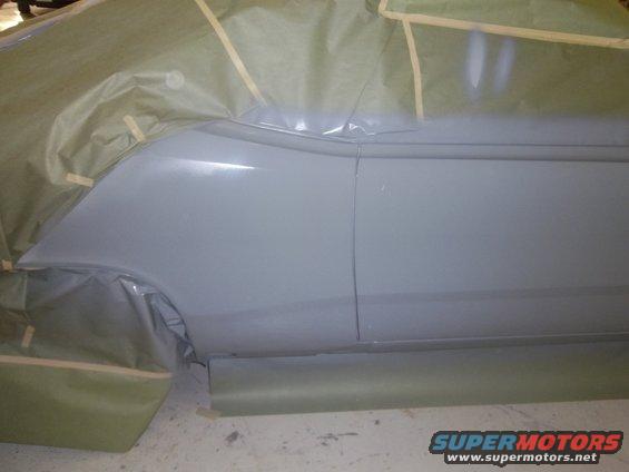 Gray car body panel covered in masking paper and tape, showing primer and a seam