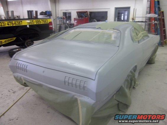 Gray 1971 Dodge Dart coupe covered in masking paper and primer, viewed from the rear