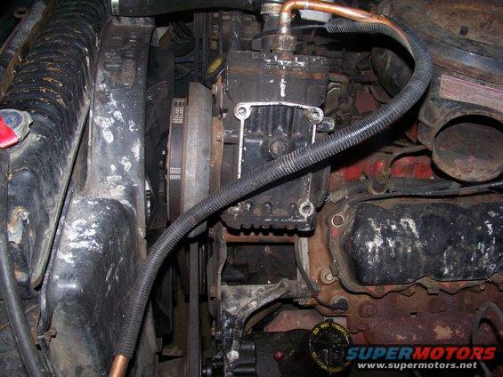 Engine bay with visible belts, pulleys, and engine block. Some hoses and a black compressor unit are also present