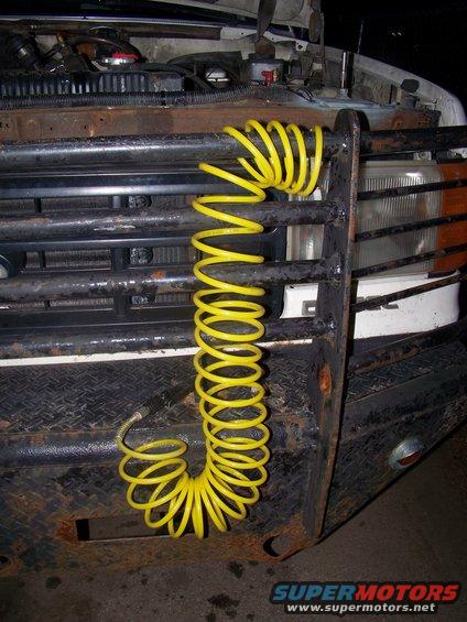Front grille of a truck with a yellow coiled air hose hanging from it. Headlights and part of the hood are visible
