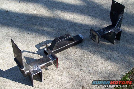 Two fabricated steel brackets on concrete, one with a vertical plate, the other with a horizontal plate