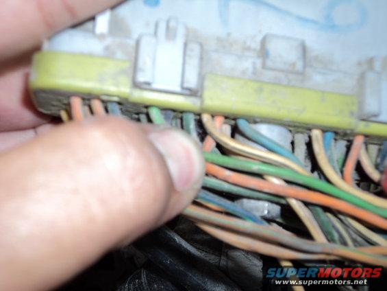 Close-up of a hand touching a yellow and white electrical connector with multiple colored wires