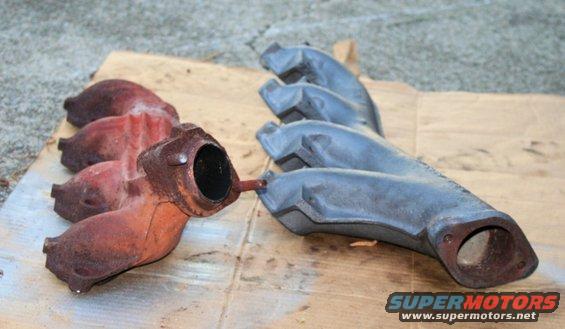 Two exhaust manifolds, one rusted red, the other painted gray, lying on cardboard