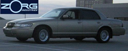 Tan 2000 Mercury Grand Marquis sedan, side view. Zorg Industries logo in upper left