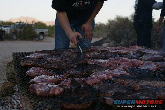 People grilling large amounts of meat outdoors