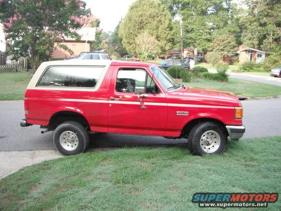 Red 1989 Ford Bronco parked on grass next to a street