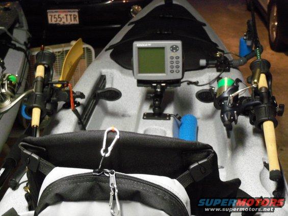 Kayak rigged for fishing with rods, reel, and fish finder. A license plate is visible in the background