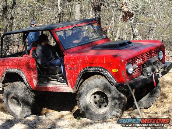 Red SUV with off-road tires and a winch on the front bumper, driving on a dirt trail with trees in the background