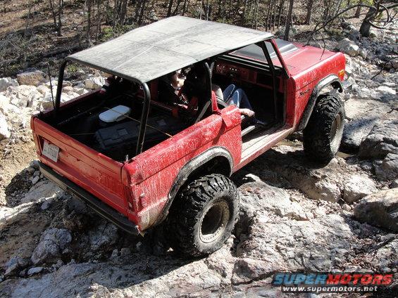 Red SUV with large tires navigating rocky terrain. Roll cage and open doors visible