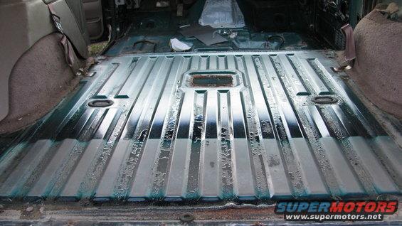 Interior floor of a vehicle undergoing restoration, showing ribbed metal flooring and removed seats
