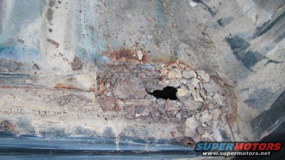 Heavily rusted and corroded vehicle floor pan with a large hole