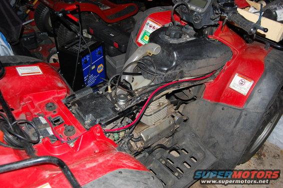 Close-up of a red ATV engine with a battery charger and lawnmowers in the background