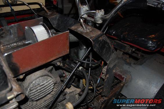 Close-up of an ATV engine, air filter, and seat. Some wiring and metal brackets are visible