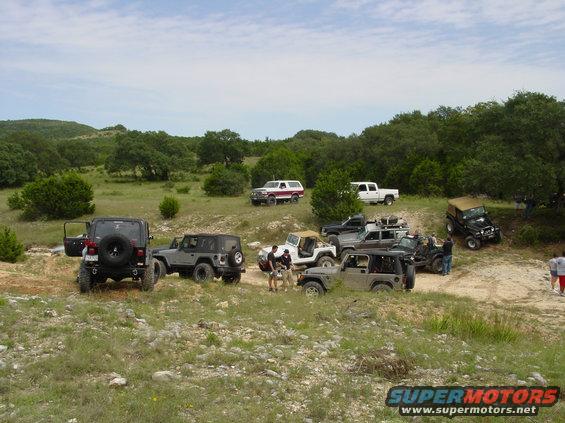Several Jeeps parked on a dirt trail with trees and hills in the background