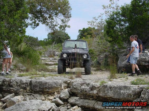 Black off-road vehicle on rocky terrain with people nearby