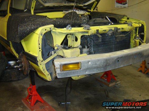 Front of a yellow car on jack stands, hood open, bumper removed