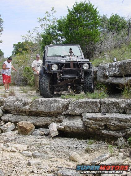 Black off-road vehicle with large tires and a roll bar, parked on rocky terrain