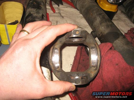 Hand holding a rusty driveshaft U-joint with visible wear marks. Red shop rag underneath