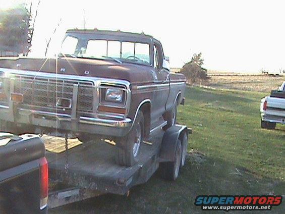 Maroon Ford F-Series truck on a trailer, front 3/4 view, rusty grille, sun glare