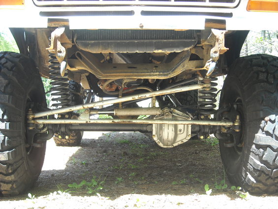 Underside view of a truck's front axle, suspension, and large tires