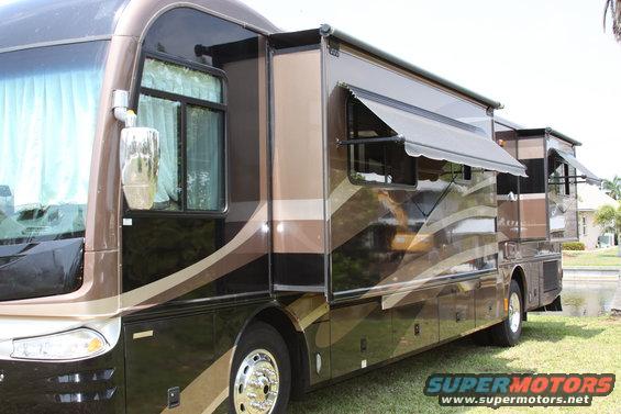Side view of a brown and tan motorhome with slide-outs extended, another motorhome visible behind it