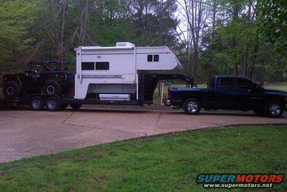 Dark pickup truck towing a trailer with a camper and an off-road vehicle on a paved surface