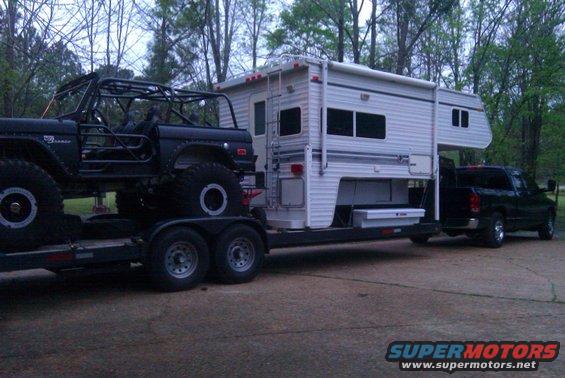 Side view of a modified black 1966 Ford Bronco on a trailer, with a camper and tow truck