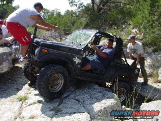 Black off-road vehicle with people on rocks, one person pulling a rope