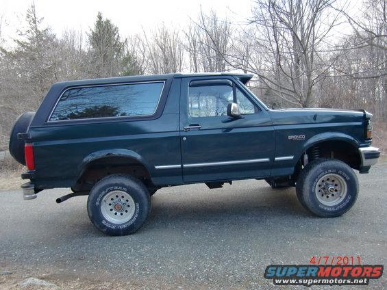 Side view of a lifted 1993 Ford Bronco, dark green with a spare tire on the rear