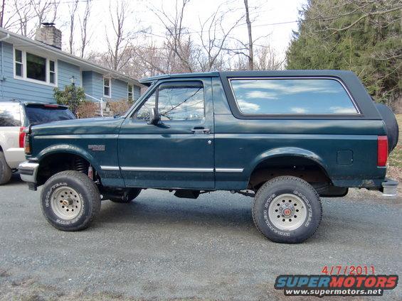 Green Ford Bronco parked outside a house. Another SUV is parked next to it