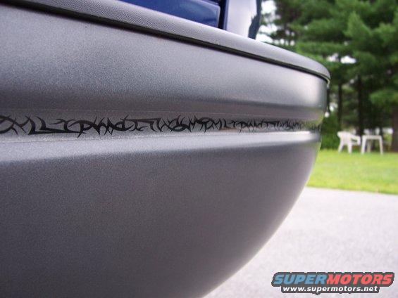 Close-up of a gray truck rear bumper with a black tribal graphic strip