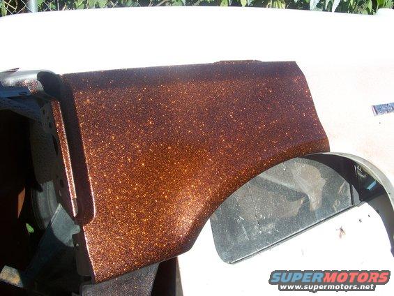 Close-up of a vehicle fender with metallic copper paint. Part of a wheel well is visible