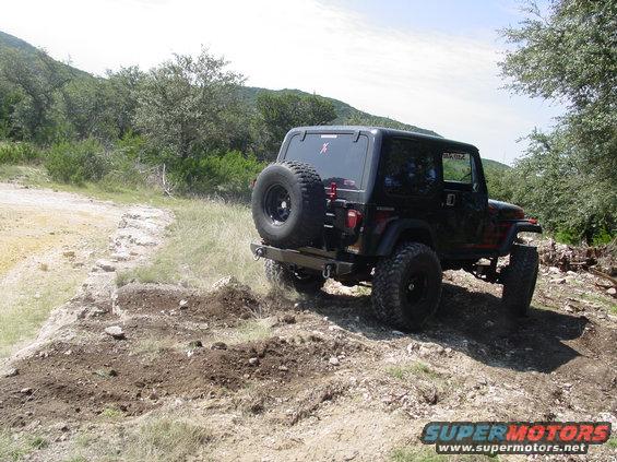 Black Jeep Wrangler TJ driving on a dirt trail with a spare tire on the back