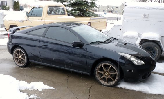 Dark coupe with aftermarket bronze wheels parked in snow. Hood has vents