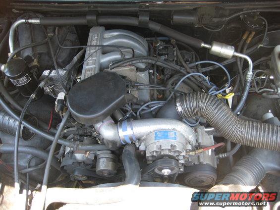 Engine bay with V8 engine, supercharger, and hoses. Supermotors.net logo visible