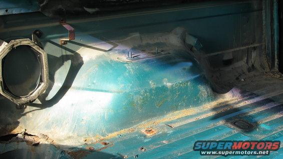1992 Ford Bronco interior floor pan, teal, showing rust and wear. Speaker housing visible on left