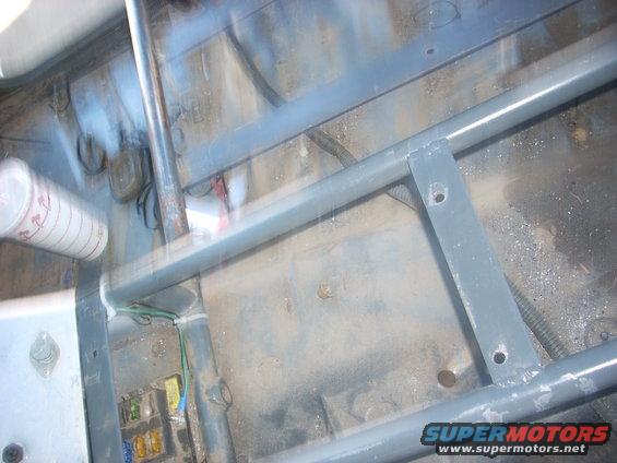 Interior of a vehicle with a roll cage, fuse box, and a cup. The floor appears to be metal