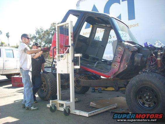 1992 Ford Ranger cab, red and black, being lifted by a hydraulic lift, with a white truck in the background
