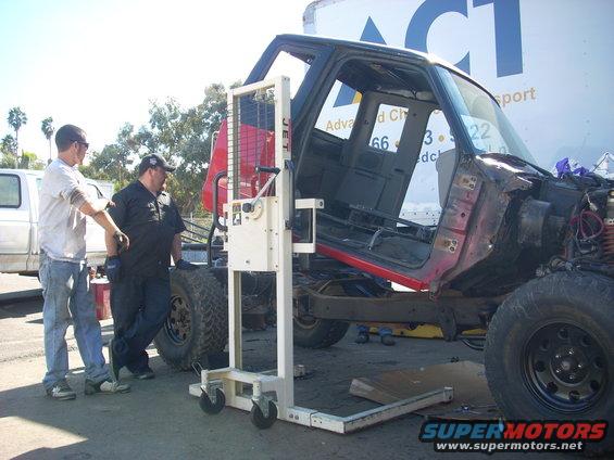Truck cab on a lift, with two men nearby. Text on trailer reads ACT