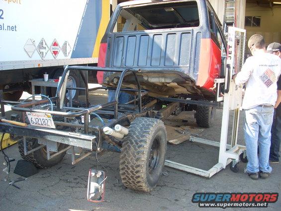 Custom off-road vehicle chassis with a truck cab being worked on next to a lift