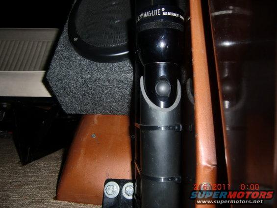 Maglite flashlight secured with zip ties next to a speaker box and brown interior panel