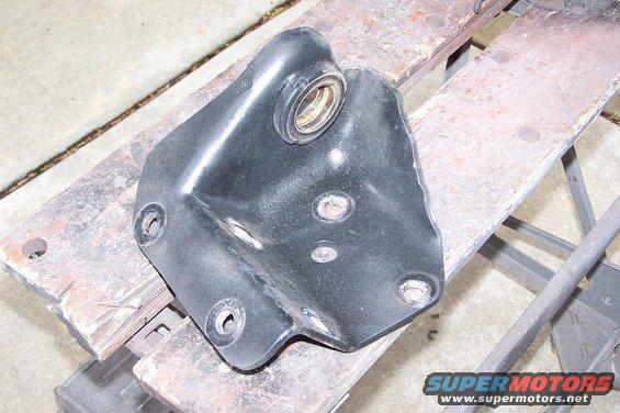 Black metal bracket with a bearing, resting on a wooden surface. Multiple bolt holes are visible