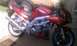 2003 Suzuki SV1000S - A red 2003 Suzuki SV1000S motorcycle is parked outside, showing its frame and aftermarket exhaust system.