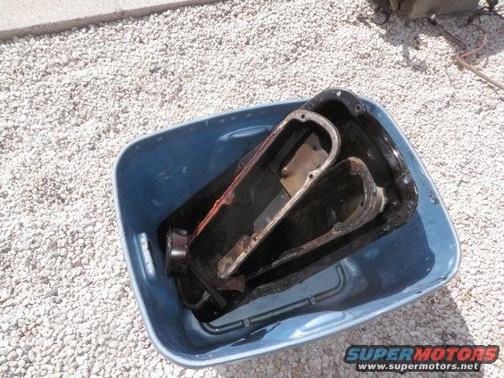 Two used oil pans submerged in water inside a blue plastic tub