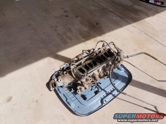Engine block with intake manifold and fuel lines on a blue plastic tray on concrete