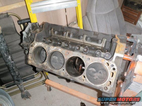 Engine block with four cylinders visible, resting on an orange engine stand