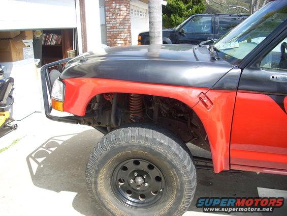 Red and black pickup truck fender and wheel, with a black brush guard